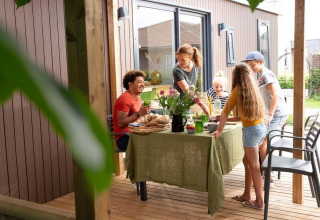 Familie isst gemeinsam auf einer Terrasse einer Family Lodge im Holiday park De Boshoek, Niederlande.