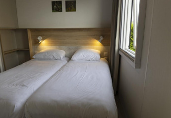 Zwei Einzelbetten in einem hellen Zimmer mit Fenster, Nachttischlampen und Holzdekor in Family Lodge.