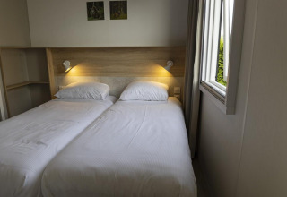 Twin beds with white linens, reading lights, and wood headboard in Family Lodge at De Boshoek, Netherlands.