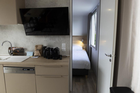 Moderne lodgekeuken met vaatwasser, koffietoestel en zicht op slaapkamer in Family Lodge De Boshoek.