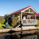 Idyllisk lodge Meine Luxe ved Tusken de Marren i Holland med folk på verandaen og ved vandkanten.