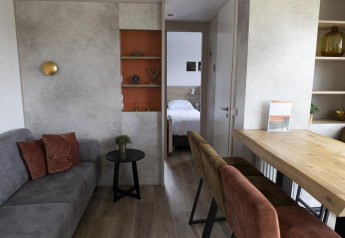 Familielodge woonkamer met zetel, eettafel, open rekken en zicht op slaapkamer bij De Boshoek, Nederland.