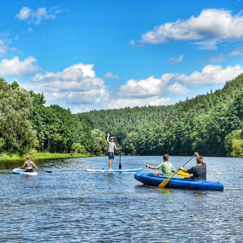 People kayaking and paddleboarding on a scenic river at Camping Prima, South Bohemia, Czech Republic, in summer.