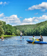 Menschen paddeln auf einem Fluss umgeben vom Wald im Camping Prima, Südböhmen, Tschechien, bei Sonnenschein.