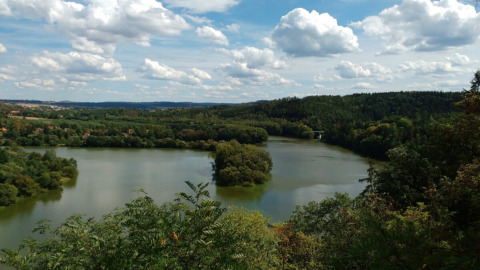 Rustige rivier en groene bossen bij Camping Prima in Zuid-Bohemen, Tsjechië, met blauwe lucht en wolken erboven.
