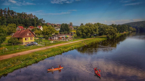 Two canoes float on a calm lake by Camping Prima, lined with houses and trees in South-Bohemia, Czech Republic.