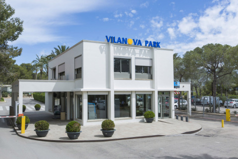 Zona de entrada al camping Vilanova Park en Cataluña, España, con edificio blanco moderno y vegetación.