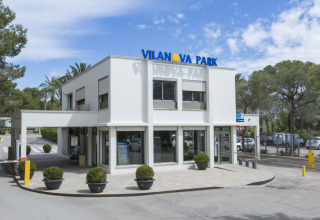 Ingangsgebied van Vilanova Park Camping in Catalonië, Spanje, met een modern, wit gebouw en planten.