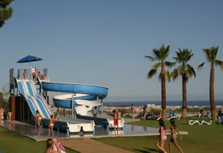 Kinder spielen an einer Wasserrutsche im Vilanova Park Campingplatz mit Palmen und Meerblick in Spanien.