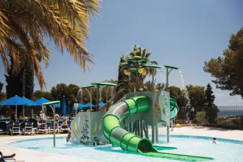 Parque acuático infantil y tobogán en el camping Vilanova Park, Cataluña, España, rodeado de palmeras.