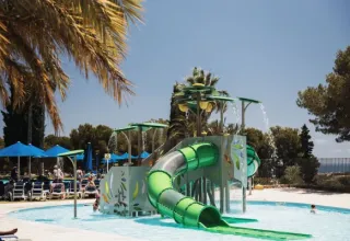 Parco acquatico per bambini con scivolo al campeggio Vilanova Park in Catalogna, Spagna, circondato da palme.