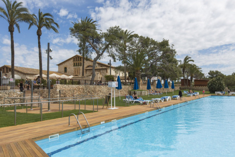 Piscina exterior con tumbonas y palmeras en el camping Vilanova Park de Cataluña, España.