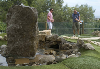 To mænd spiller minigolf ved en klippe og en vandfunktion i Vilanova Park Campsite i Catalonien, Spanien.