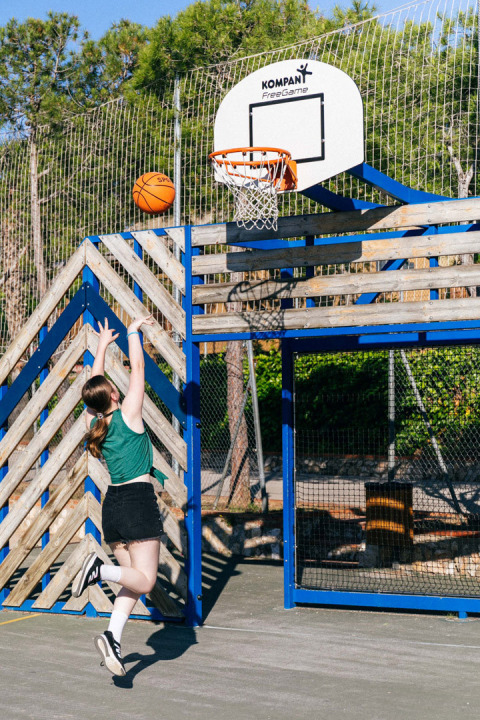 Una joven salta para lanzar una pelota de baloncesto en una cancha exterior de Vilanova Park en Cataluña.