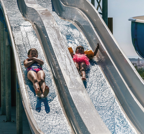 Due bambini scivolano sugli scivoli d’acqua al campeggio Vilanova Park, Catalogna, Spagna, in una giornata di sole.