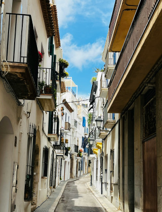 Calle estrecha con edificios blancos y balcones floridos en Vilanova i la Geltrú, Cataluña, España.