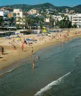 Playa de Vilanova i la Geltrú, Cataluña, España, con bañistas, sombrillas y edificios al fondo.