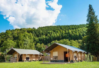 Two modern tents at Camping Village Sy holiday park in Liège, Belgium, set against green forested hills and sky.