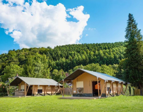 Two modern tents at Camping Village Sy holiday park in Liège, Belgium, set against green forested hills and sky.