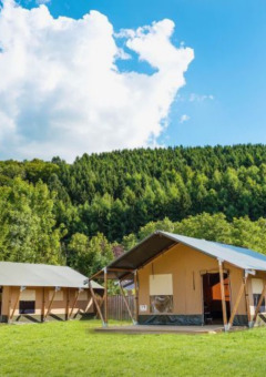 Two modern tents at Camping Village Sy holiday park in Liège, Belgium, set against green forested hills and sky.