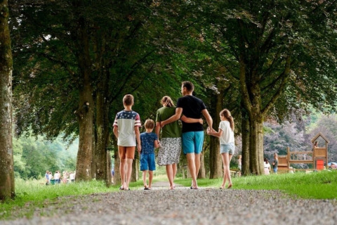 Una famiglia cammina mano nella mano su un sentiero alberato al Camping Village Sy a Liegi, Belgio.