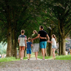 A family walks hand in hand down a tree-lined path at Camping Village Sy holiday park in Liège, Belgium.
