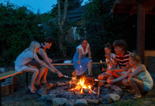Familie hygger sig rundt om bålstedet og rister skumfiduser i Camping Village Sy, Liège, Belgien.