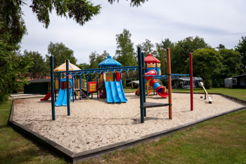 Parque infantil con toboganes coloridos y columpios sobre arena en Camping de Zeven Heuveltjes, Drenthe.