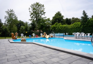 Piscina all'aperto con personaggi per bambini e sedie, circondata da alberi al Camping de Zeven Heuveltjes, Drenthe.