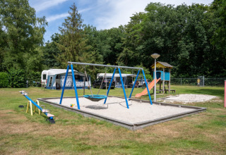 Legeplads med gynger, vippe og rutsjebane foran campingvogne på Camping de Zeven Heuveltjes i Drenthe.