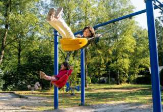 Due bambini giocano sulle altalene nel parco giochi soleggiato di Camping de Zeven Heuveltjes, Drenthe, Paesi Bassi.