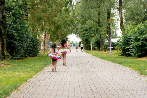 Dos niños con flotadores caminan por un sendero arbolado en Camping de Zeven Heuveltjes, Drenthe, Países Bajos.