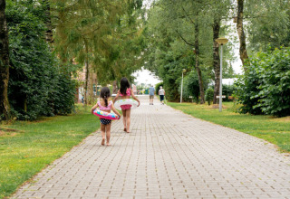 Due bambine con salvagenti camminano su un sentiero alberato nel Camping de Zeven Heuveltjes, Drenthe.