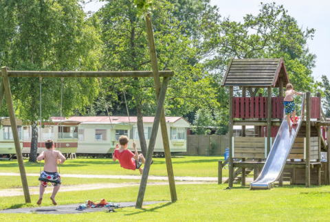 Niños juegan en columpios y un tobogán en el parque infantil de Camping Tussen de Diepen, Overijssel, Países Bajos.