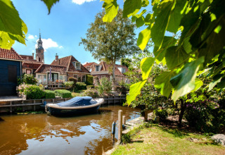 Boat on the canal near houses with gardens at Camping Tussen de Diepen holiday park, Overijssel, Netherlands.