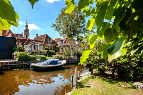 Barco en el canal junto a casas y jardines en Camping Tussen de Diepen, parque vacacional en Overijssel, Países Bajos.