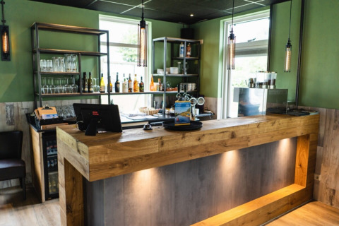 Modern bar with wooden counter, shelves of glasses and bottles at Camping Tussen de Diepen in Overijssel, Netherlands.