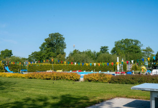 Outdoor swimming pool and playground with colorful bunting at Camping Tussen de Diepen, Overijssel, Netherlands.