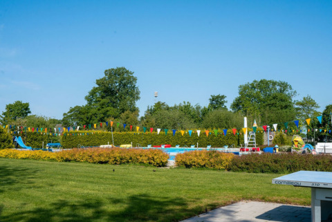 Outdoor swimming pool and playground with colorful bunting at Camping Tussen de Diepen, Overijssel, Netherlands.