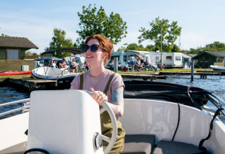 Donna che guida una barca a Camping Tussen de Diepen a Overijssel, Paesi Bassi, con roulotte sullo sfondo.