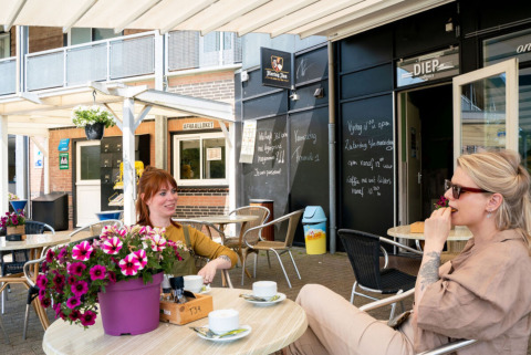 Two women relax with coffee on the terrace at Camping Tussen de Diepen holiday park in Overijssel, Netherlands.