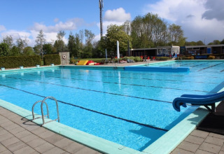 Outdoor swimming pool at Camping Tussen de Diepen in Overijssel, Netherlands, with slide and clear sky.