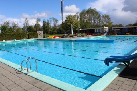 Outdoor swimming pool at Camping Tussen de Diepen in Overijssel, Netherlands, with slide and clear sky.