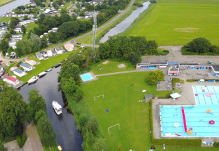 Aerial view of Camping Tussen de Diepen with swimming pools, green fields, and a canal in Overijssel, Netherlands.