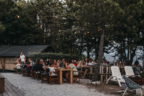 Outdoor communal dining under string lights among trees at Camping Luna del Monte holiday park in Umbria, Italy.
