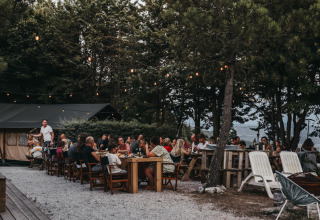 Cena all'aperto sotto alberi e luci al Camping Luna del Monte, parco vacanze in Umbria, Italia.