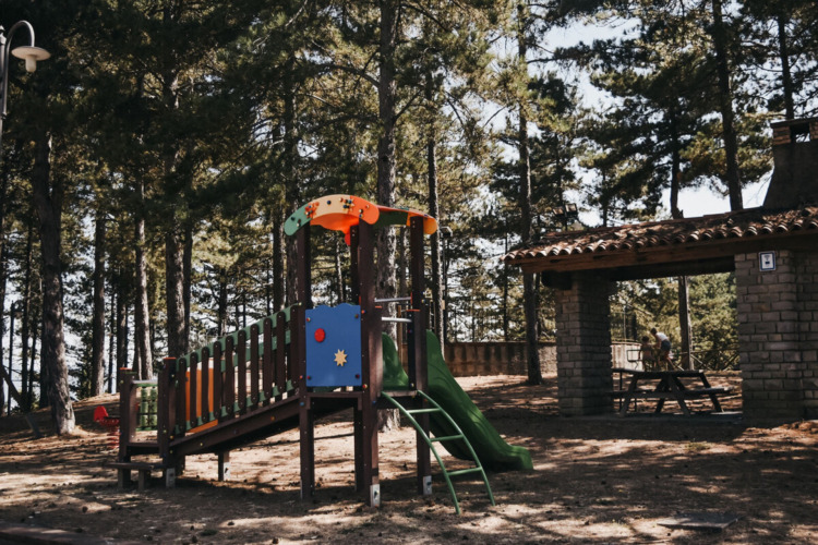 Spielplatz im Wald bei Camping Luna del Monte in Umbrien, Italien, mit Rutsche und Picknickbereich.