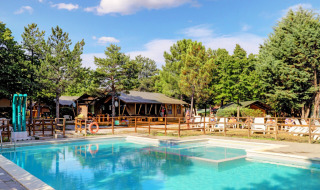 Swimming pool and sun loungers surrounded by trees at Camping Luna del Monte holiday park in Umbria, Italy.