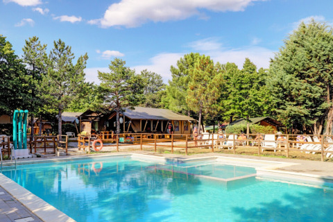 Swimming pool and sun loungers surrounded by trees at Camping Luna del Monte holiday park in Umbria, Italy.