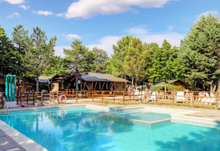 Swimming pool and sun loungers surrounded by trees at Camping Luna del Monte holiday park in Umbria, Italy.